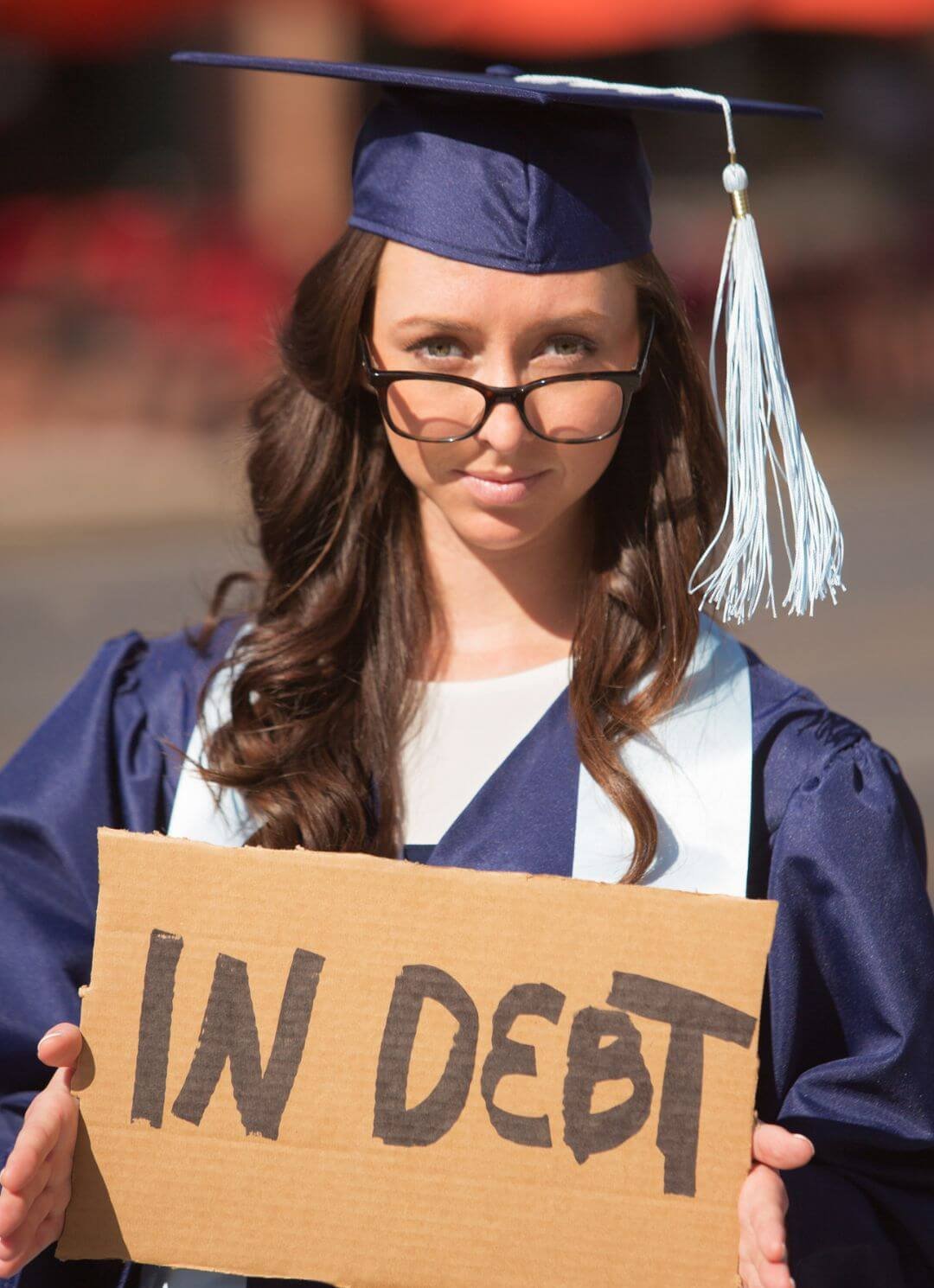 Graduate holding 'in debt' sign representing student loan debt and need for debt settlement enrollment services